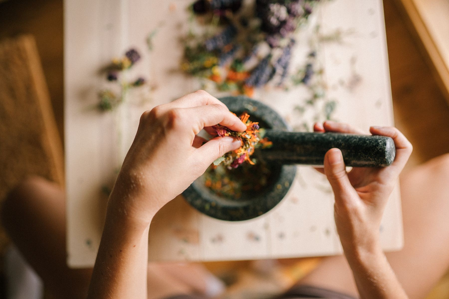 Hands grinding dried flowers and herbs in a stone mortar